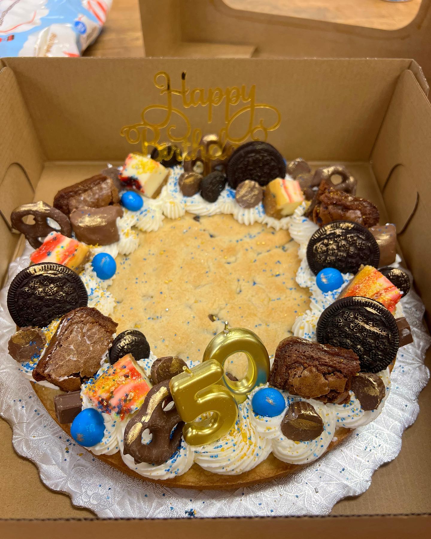 Birthday cake with chocolate cookies, candies, and a number 50 decoration in a cardboard box.