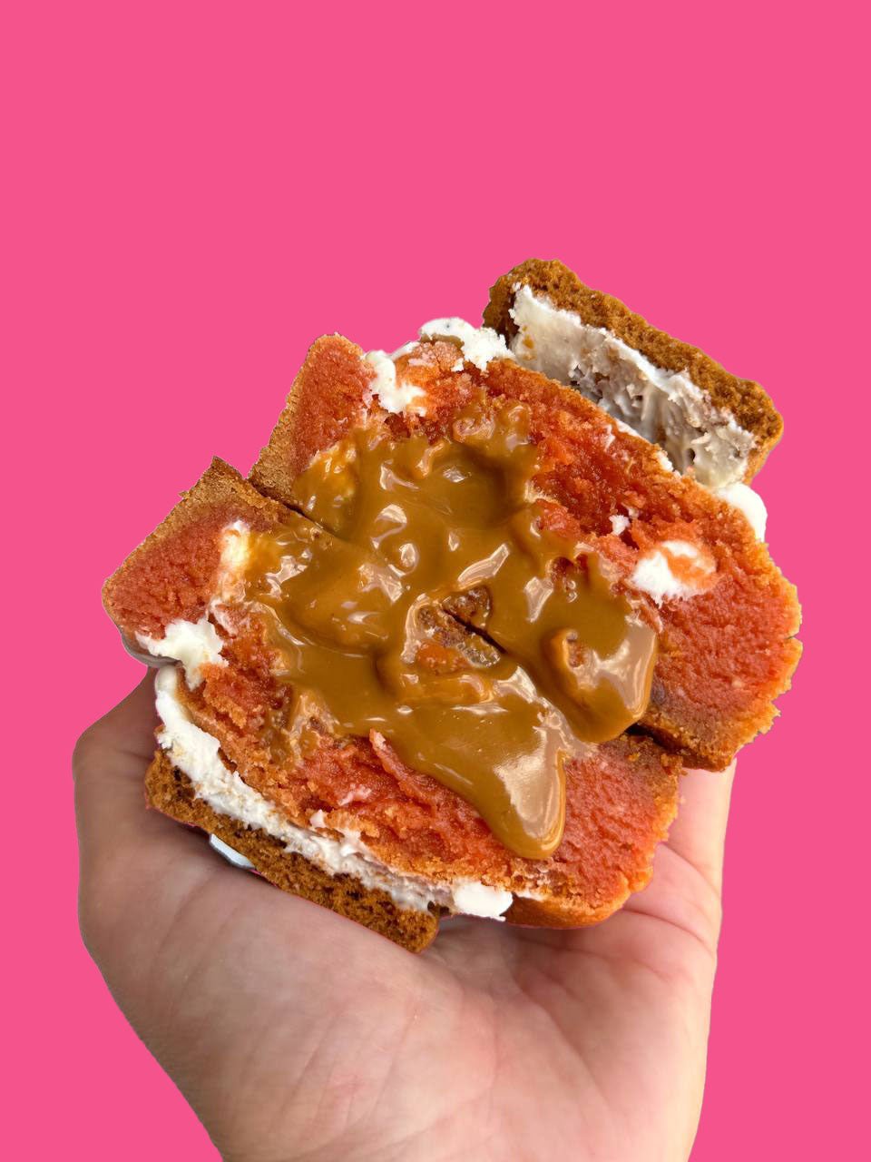 A pumpkin flavored cookie being held against a pink background.