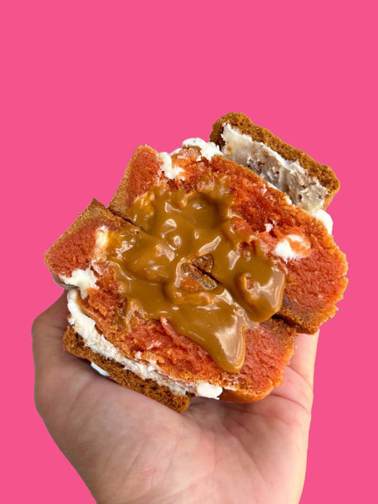 A pumpkin flavored cookie being held against a pink background.