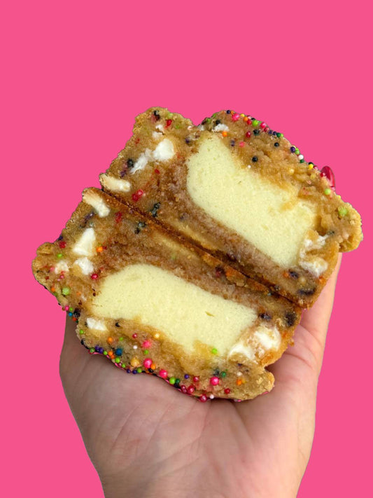 A cheesecake stuffed confetti cookie being held against a pink background.