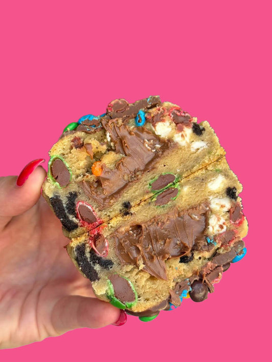 A candy and chocolate stuffed cookie being held against a pink background.