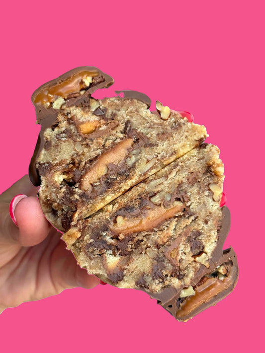 A gourmet chocolate cookie being held against a pink background.